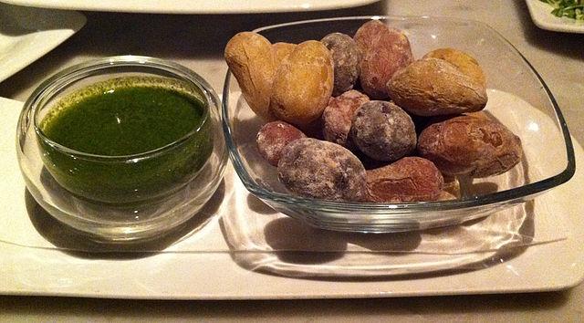 Papas arrugadas con un mojo verde en un cuenco al lado.