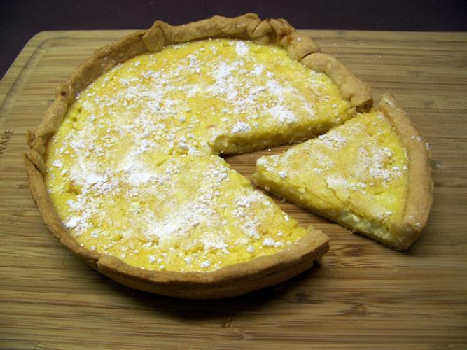 Una tarta de requesón y crema de limón sobre una tabla de madera con un trozo cortado.