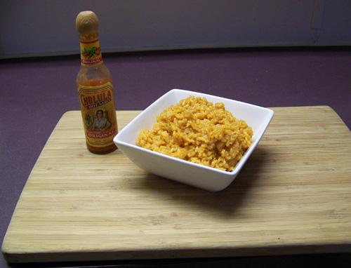 Un recipiento con arroz al estilo mexicano sobre una mesa con una botella de salsa al lado.