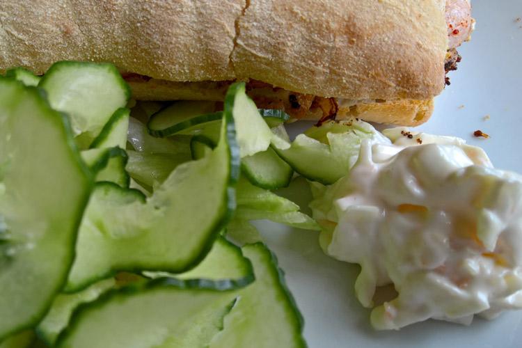 Bocadillo de pollo y tocino con rodajas de pepino y coleslaw.