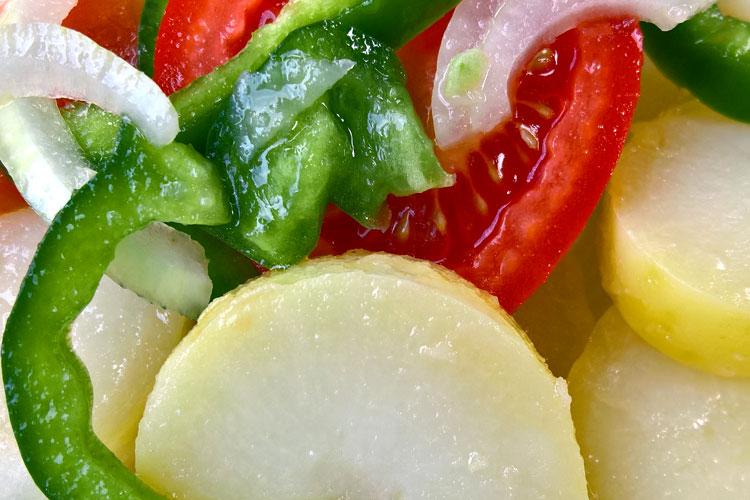 Detalle de una ensalada campera con patata, tomate, pimiento, cebolla y vinagreta.