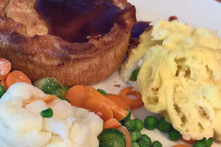 Pastel de carne y riñones servido con puré de patatas, vreduras y salsa.