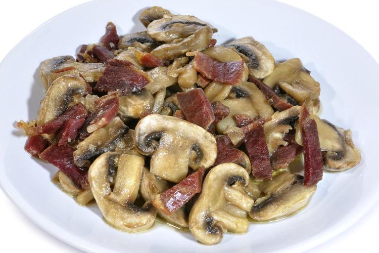 Un plato de champiñones salteados con jamón serrano.