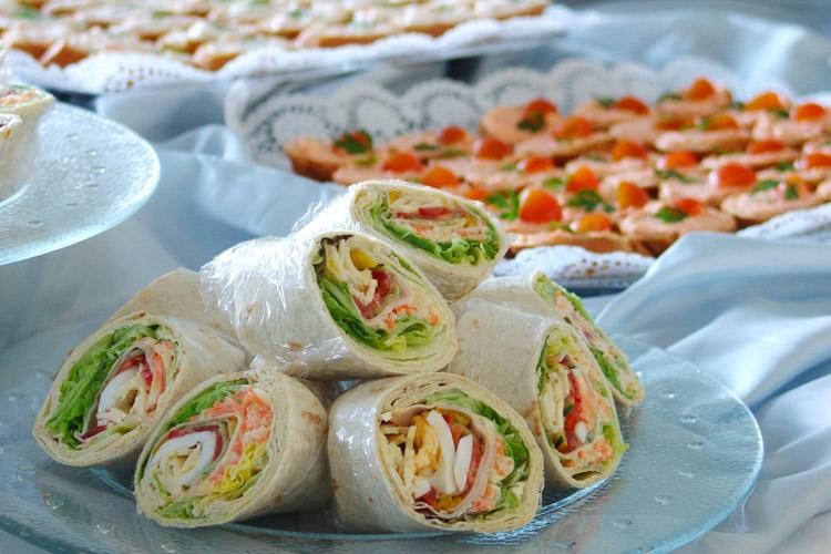 Bocadillos y canapés sobre mesa con mantel blanco.