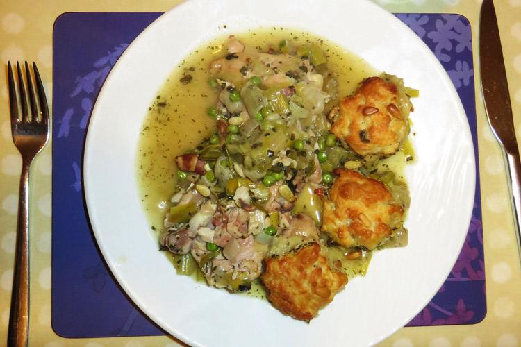 Una ración de cazuela de pollo al pesto con bolas de queso y piñones servida en plato.