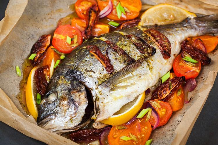 Una fuente con un besugo al horno y sus guarniciones.