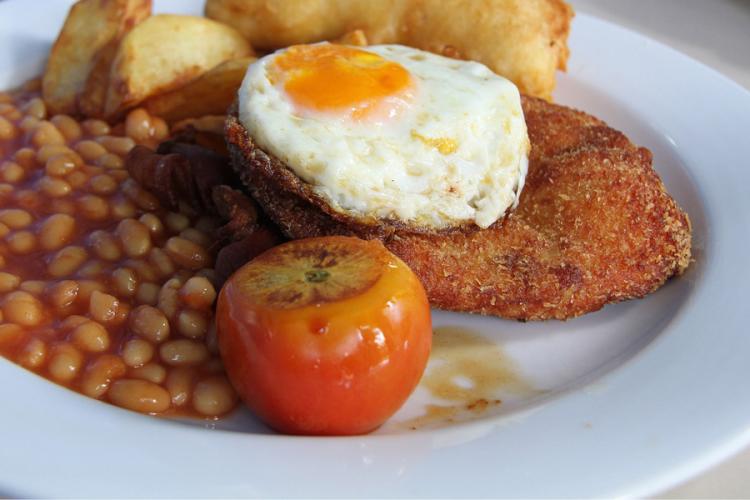 Plato de pollo empanado con un huevo a caballo, alubias al horno y patatas fritas.