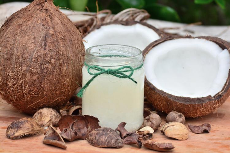 Un coco entero, aceite de coco en un vaso de vidrio y un coco partido por la mitad.