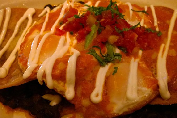 Huevos rancheros con frijoles refritos, salsa roja, nata y salsa cruda.