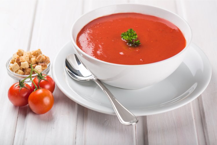 Sopa de tomate en un cuenco blanco sobre mesa de madera.