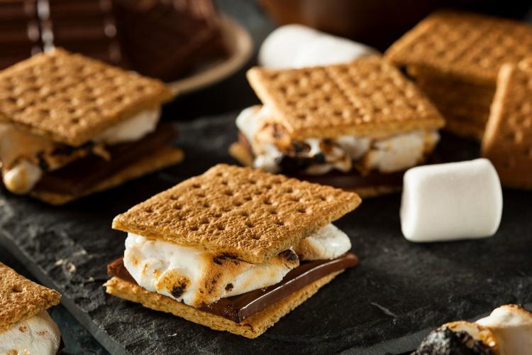 S´mores con Graham crackers, chocolate y malvavisco blanco sobre una mesa negra.