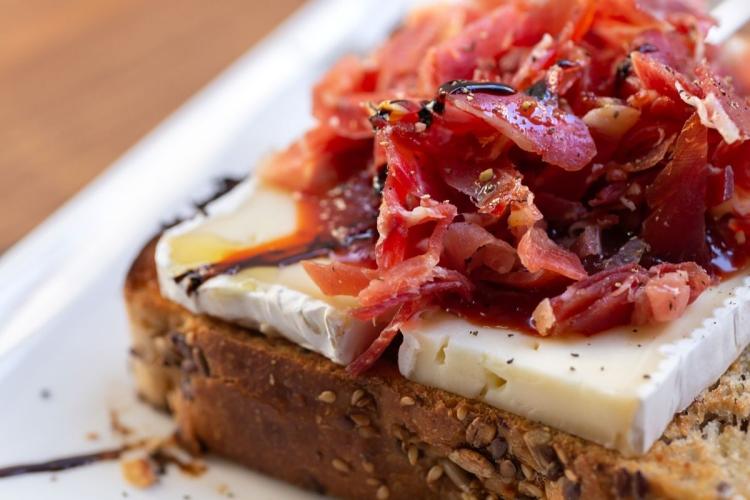 Tostada con queso brie, jamón serrano y confitura de tomate.