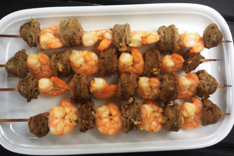 Brochetas de gambas y salchicha en una fuente de loza.