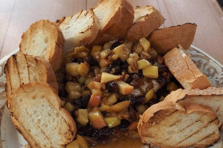 Queso brie al horno con manzana, pacanas y pasas fritas en mantequilla con licor.