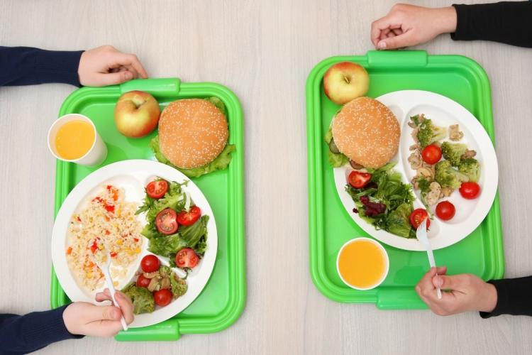 Dos niños con bandejas de comida en el comedor escolar.