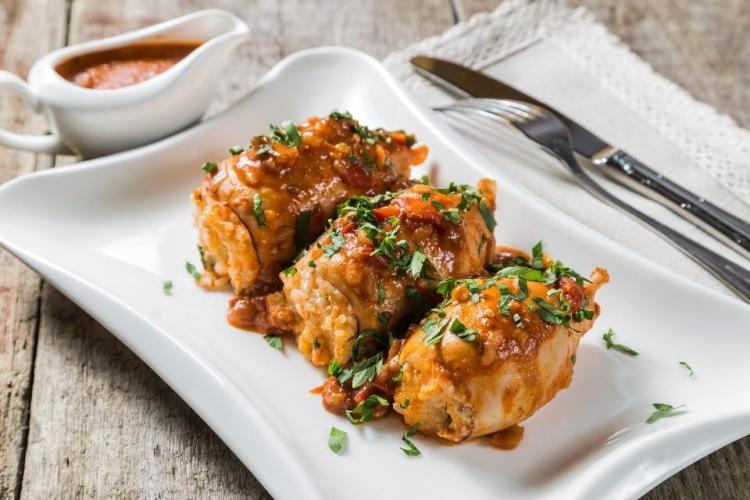 Un plato con tres calamares rellenos de arroz servidos con salsa de tomate en salsera.