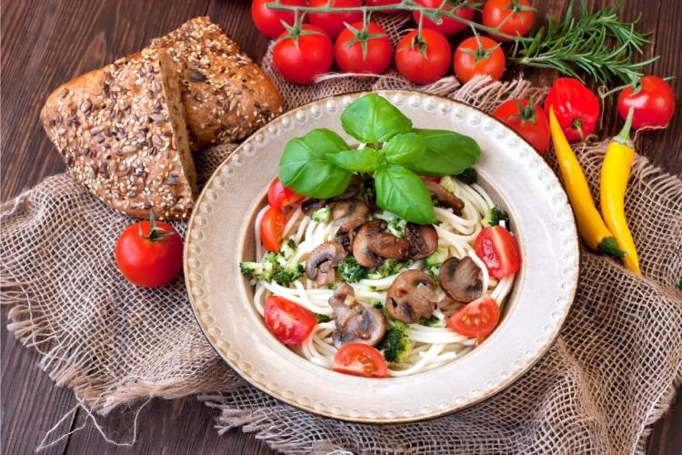 Espagueti con brócoli y champiñones y guarnición de tomates frescos.