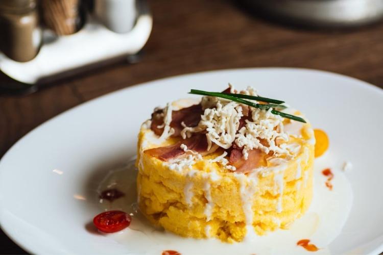 Polenta con prosciutto, queso rallado y salsa en forma de torre redonda.