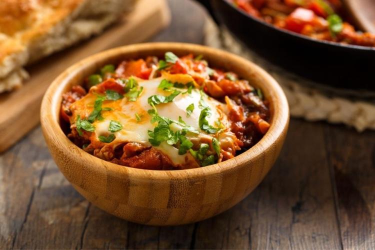 Shakshuka con huevo servida en un bol de madera.