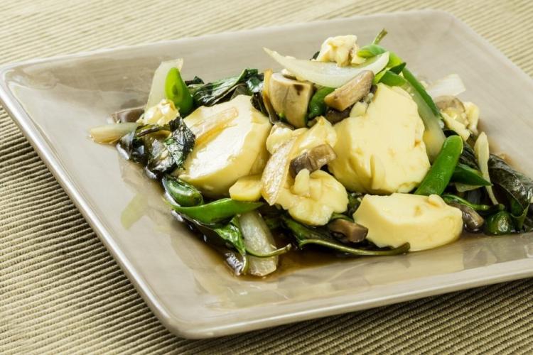 Un plato cuadrado con tofu salteado con albahaca y salsa de soja.
