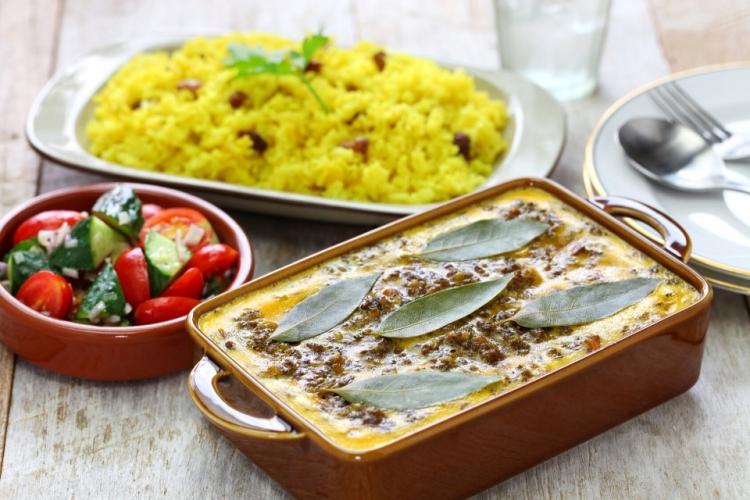 Una fuente con bobotie recién hecho acompañada un cuenco de sambal y una fuente de arroz pilau.