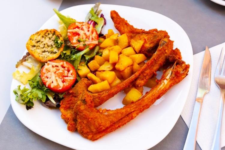 Chuletas de cordero empanadas con patatas fritas y ensalada.