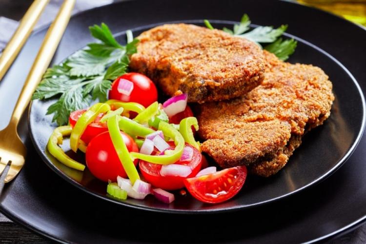 Dos chuletas sin palo de cordero empanado con ensalada de tomate.
