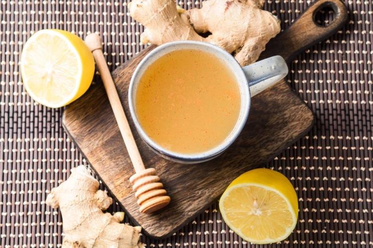 Una taza de infusión de jengibre fresco, miel y limón sobre tabla de madera.