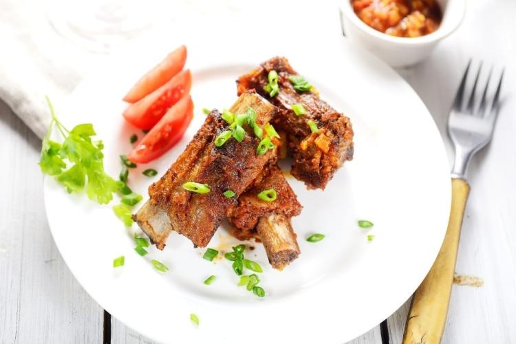 Un plato con costillas de cerdo aromatizadas y fritas acompañadas de tomate y decoradas con cebollino.