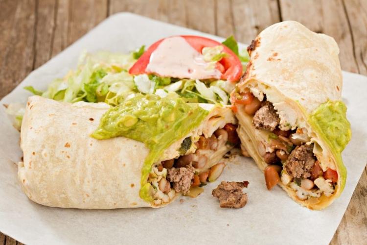 Burrito de carne servido con guacamole por encima y acompañado con ensalada.