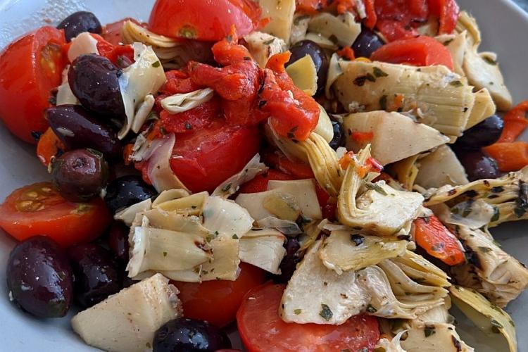 Ensalada de alcauciles con pimientos rojos, aceitunas y aliño a las hierbas.