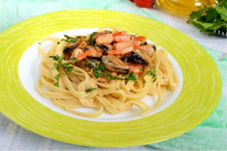 Cintas con marisco presentada en un plato de loza con borde de color verde pálido.