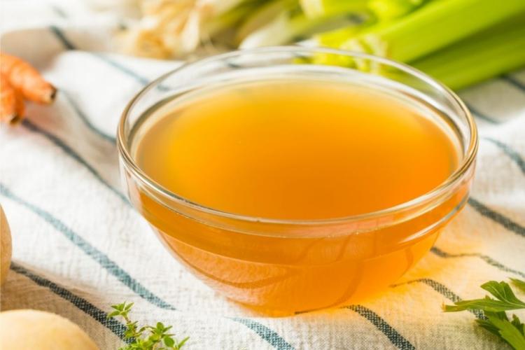 Un cuenco de vidrio con caldo de verduras rodeado de algunos de los ingredientes.