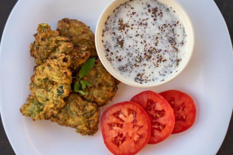 Tortitas de calabacín acompañadas de salsa de yogur y rodajas de tomate.