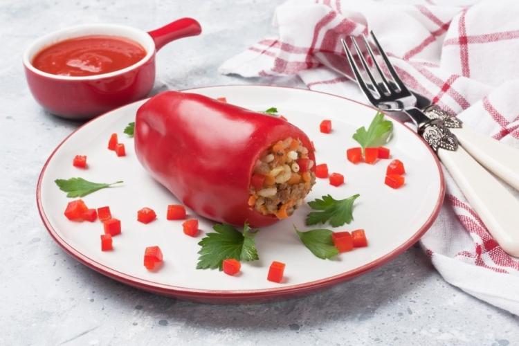Un plato con un pimiento parecido a los pimientos de piquillo relleno decorado con pimiento picado.