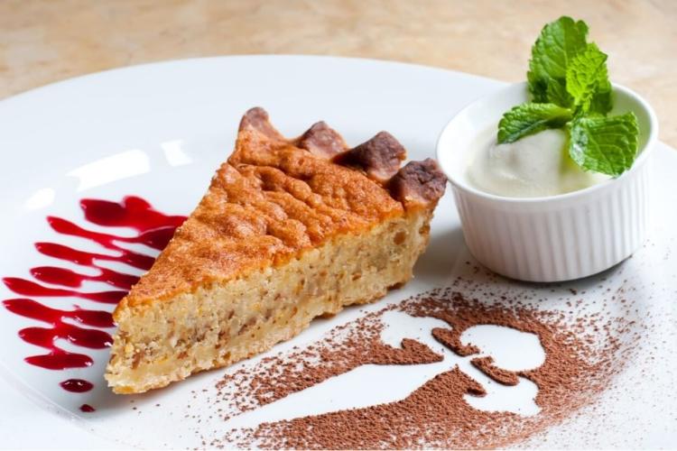 Un trozo de tarta de Santiago con coulis de frambuesa, helado y cacao en polvo.
