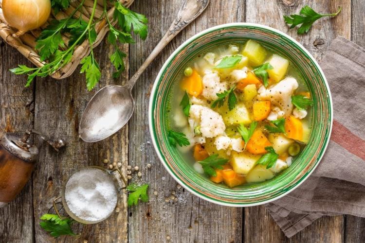 Un taz'on con sopa de verduras sobre madera.