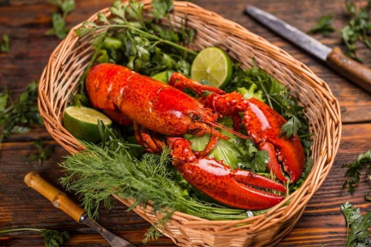 Una langosta cocida en una cesta con hierbas aromáticas y una lima.