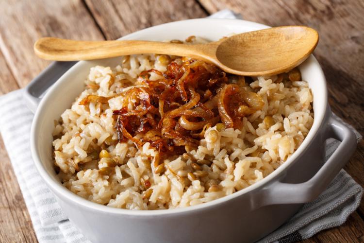 Plato hondo de cerámica con mujaddara, una mezcla de arroz y lentejas, coronado con cebollas caramelizadas y acompañado de una cuchara de madera.
