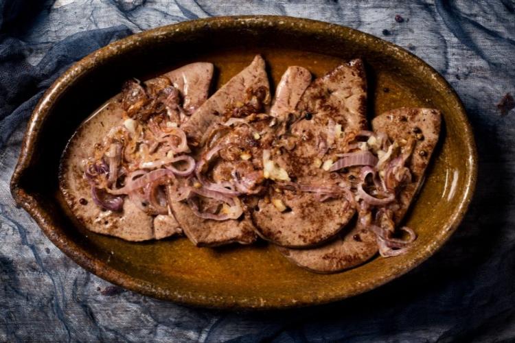 Cuatro filetes de hígado encebollado en una fuente de barro.