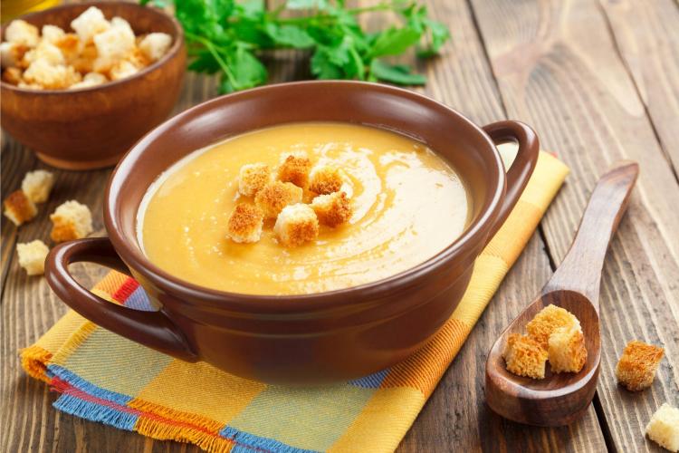 Puré de lentejas rojas, zanahoria y batata en un cuenco, acompañado de cuscurros de pan.