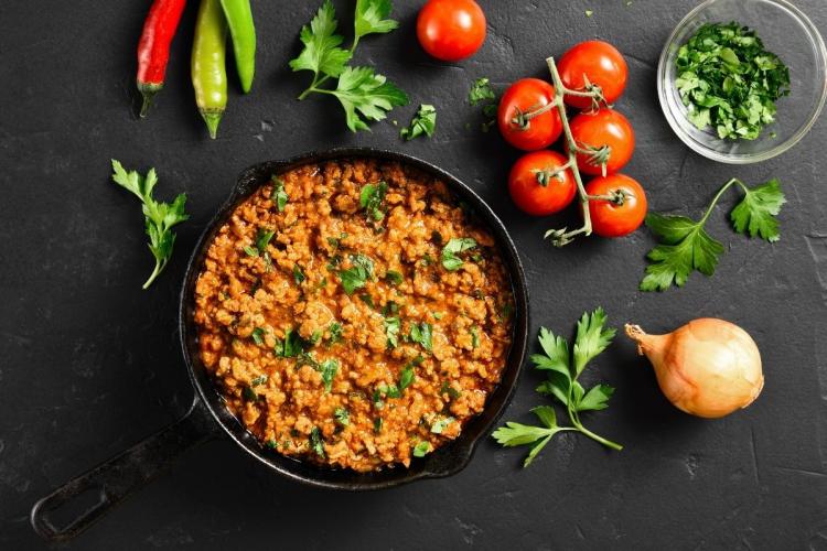 Curry kima en una sartén de hierro rodeado de algunos de sus ingredientes.
