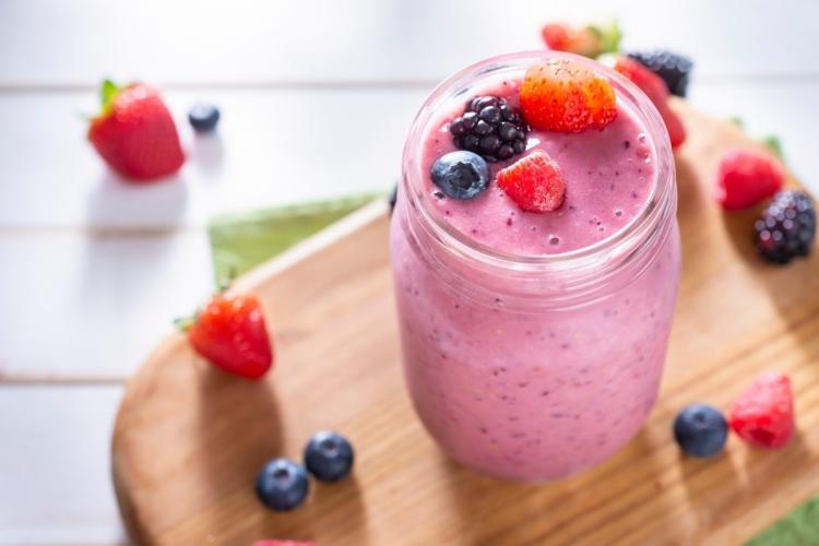 Batido de frutos del bosque en un vaso con algunos frutos del bosque frescos alrededor.