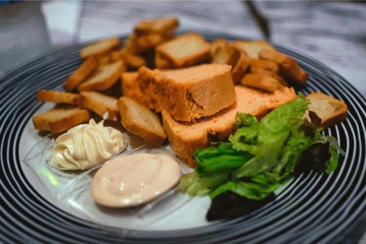 Rodajas de pastel de cabracho acompañado de tostadas de pan y salsa mahonesa en cuencos.