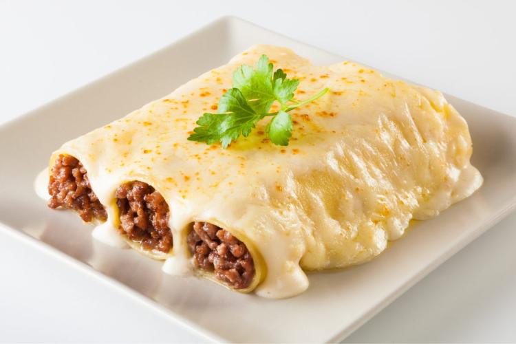 Un palto cuadrado con tres canelones de carne cubiertos de salsa de queso.