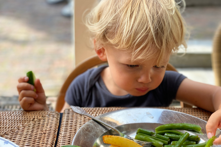NIño pequeño comiendo verduras con las manos.