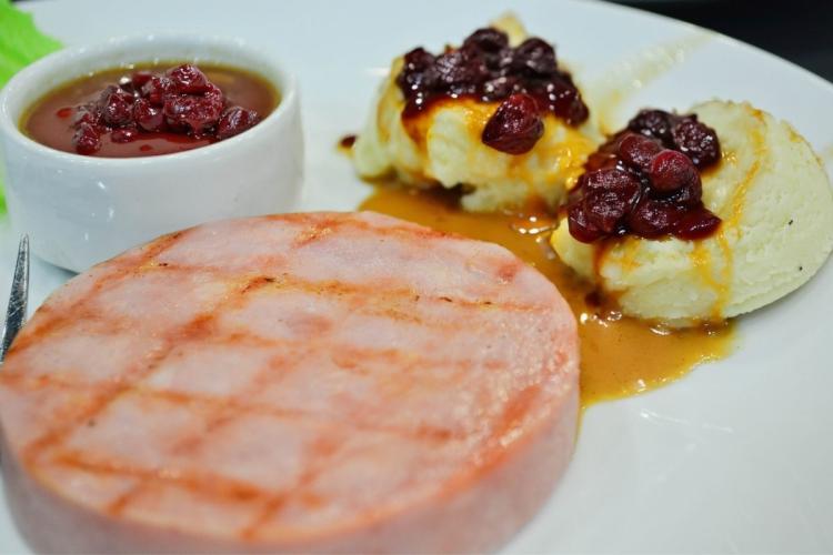 Un plato con una loncha de jamón asado, puré de patata y salsa de guindas.
