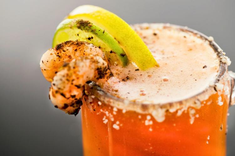 Un vaso de michelada escarchado con sal y decorado con colas de camarones, una rodaja de lima y una rodaja de limón.