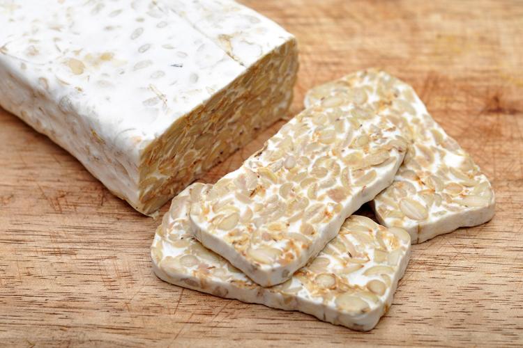 Un bloque de tempeh fresco y tres rebanadas ya cortadas sobre una tabla de madera.