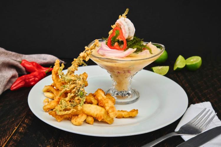 Una copa de leche de tigre, bien decorada, acompañada de chicharrón.